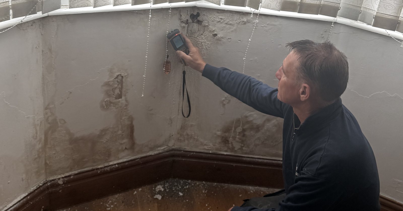 Surveyor taking a moisture meter reading on a wall showing tide marks and salt staining