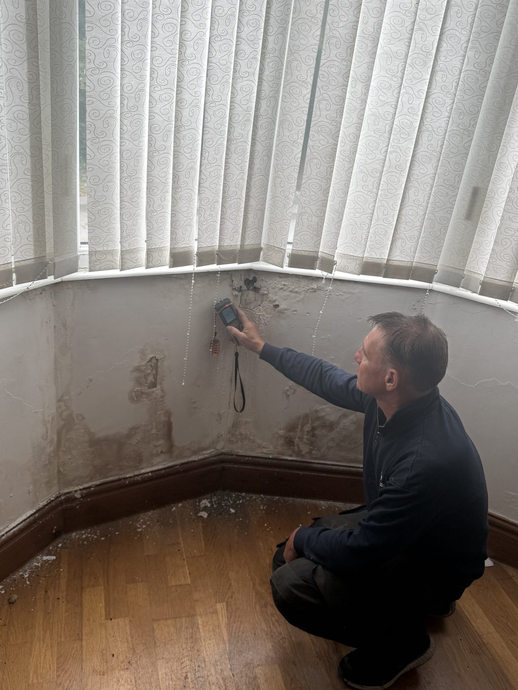 Surveyor taking a moisture meter reading on a wall with tide marks and spalled plaster