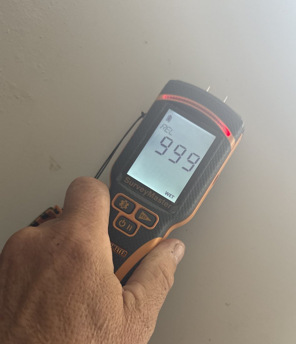 A moisture meter held against a wall, reading 999 with the WET indicator lit